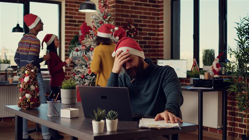 OSM Thome — Employee-being-frustrated-by-christmas-holiday-festivity-startup-office-trying-work-laptop-xmas-eve-time-stressed-man-being-disturbed-interrupted-by-noisy-people (1)